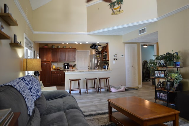 living area with ceiling fan, light wood-type flooring, visible vents, and high vaulted ceiling