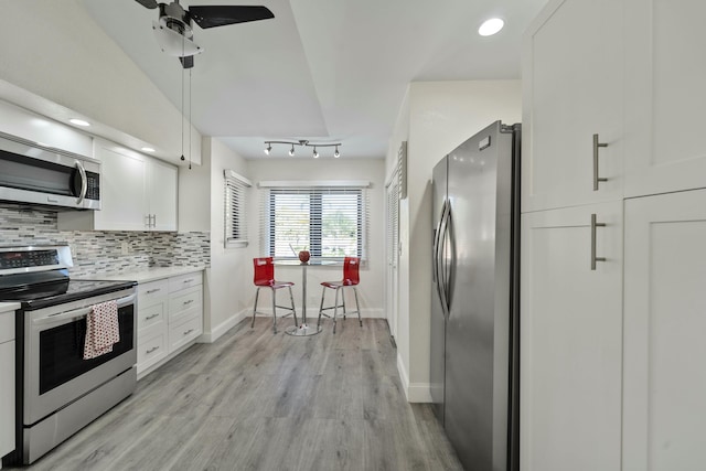 kitchen with appliances with stainless steel finishes, white cabinets, light wood-style floors, and tasteful backsplash