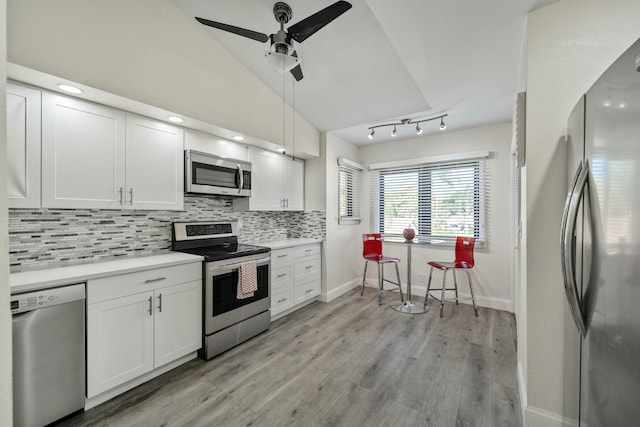 kitchen with white cabinetry, vaulted ceiling, appliances with stainless steel finishes, light wood-type flooring, and tasteful backsplash