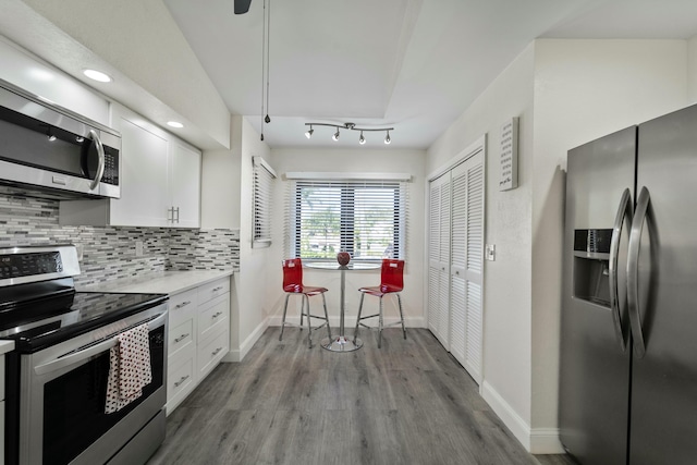 kitchen featuring stainless steel appliances, wood finished floors, white cabinets, and decorative backsplash