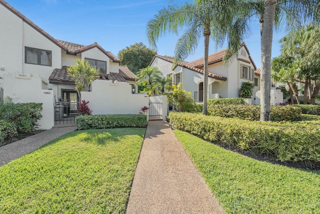 mediterranean / spanish-style house featuring a tile roof, stucco siding, a residential view, a gate, and a front yard