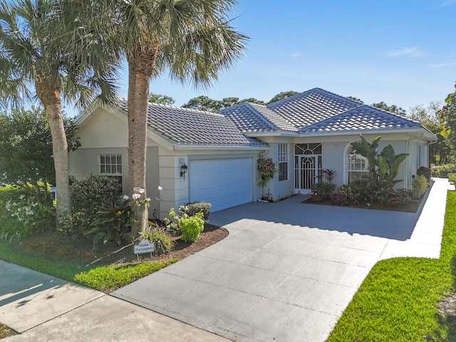 ranch-style house featuring a tiled roof, a garage, driveway, and stucco siding