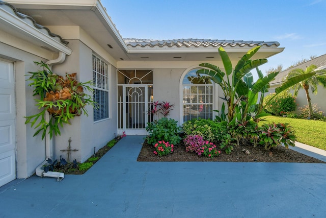 property entrance featuring a tile roof, an attached garage, and stucco siding