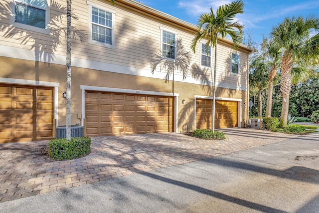 view of front facade featuring stucco siding, central air condition unit, a garage, and driveway