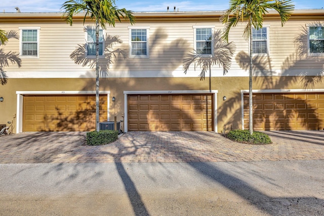 view of property featuring stucco siding, central air condition unit, an attached garage, and driveway