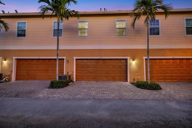 multi unit property featuring central air condition unit, an attached garage, driveway, and stucco siding