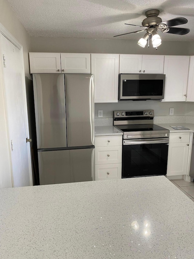 kitchen featuring a textured ceiling, stainless steel appliances, white cabinetry, and light stone countertops