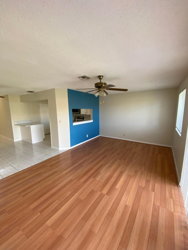 unfurnished living room with light wood-style flooring, a textured ceiling, visible vents, and a ceiling fan