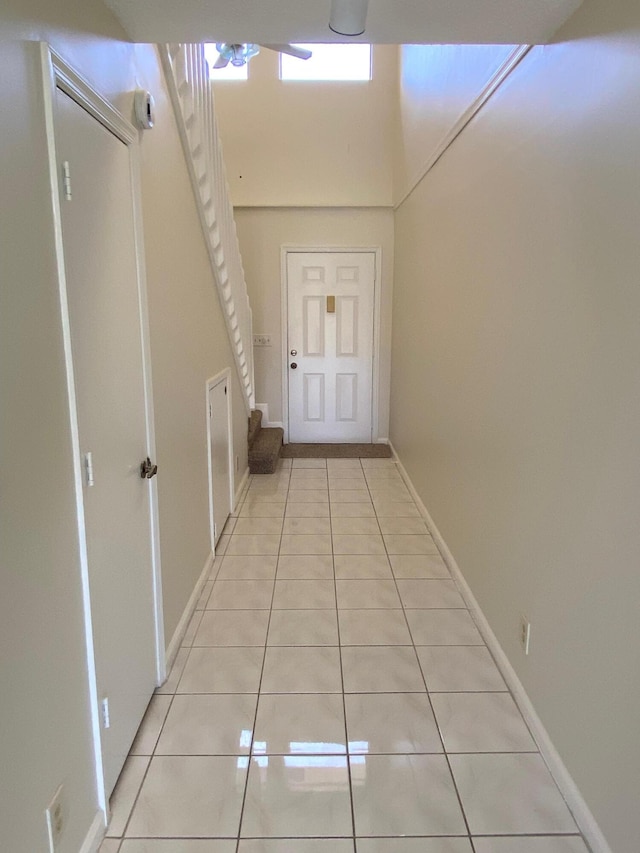 corridor featuring stairway, light tile patterned flooring, a towering ceiling, and baseboards