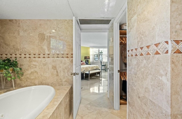 ensuite bathroom with a garden tub, tile walls, ensuite bath, and a spacious closet