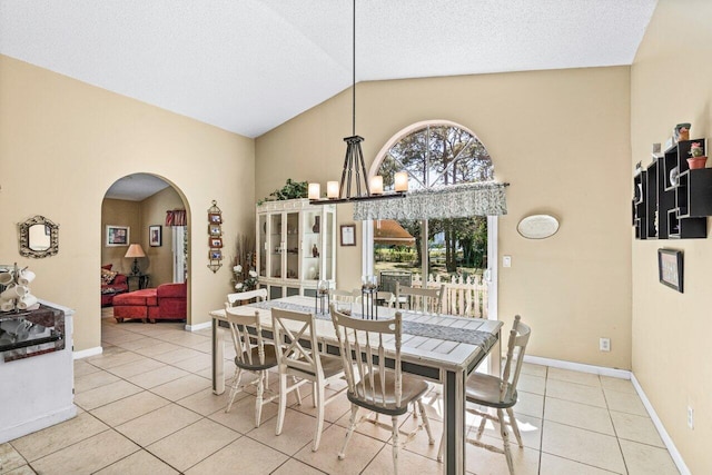 tiled dining room with baseboards, arched walkways, an inviting chandelier, a textured ceiling, and high vaulted ceiling