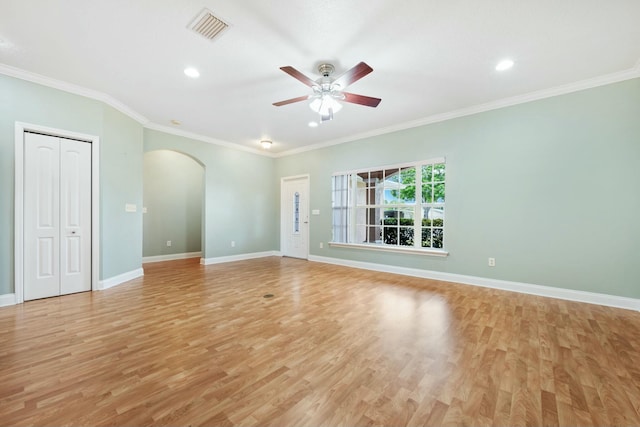 spare room with light wood finished floors, baseboards, visible vents, arched walkways, and ornamental molding