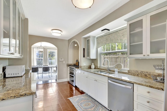 kitchen featuring arched walkways, stainless steel appliances, a wealth of natural light, and a sink