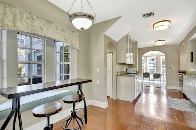 kitchen with glass insert cabinets, arched walkways, visible vents, and baseboards