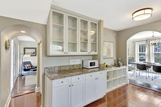 535 28th St, West Palm Beach, FL 33407 - kitchen featuring white microwave, arched walkways, dark tile patterned flooring, glass insert cabinets, and a chandelier