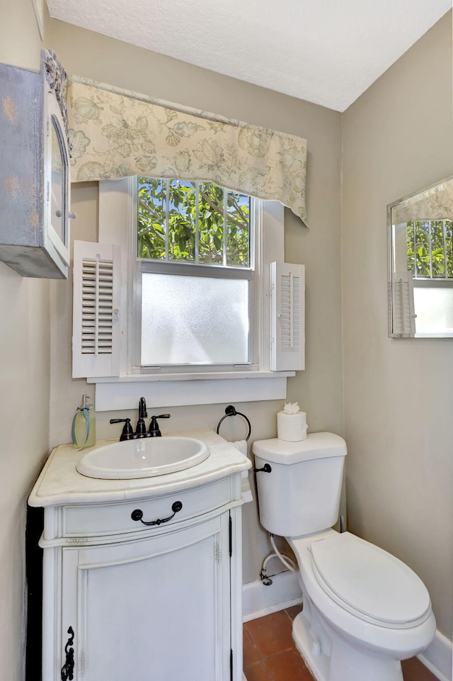 half bathroom with vanity, toilet, baseboards, and tile patterned flooring