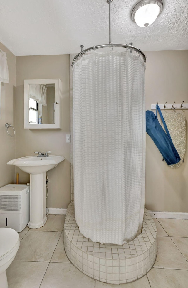 bathroom with a shower with curtain, toilet, a textured ceiling, tile patterned flooring, and baseboards