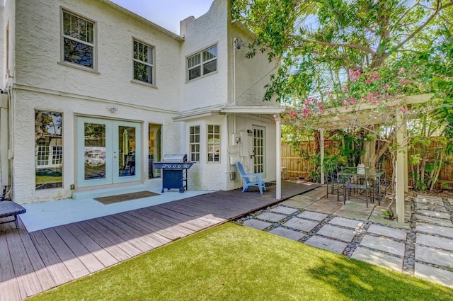 back of property featuring fence, a wooden deck, stucco siding, french doors, and outdoor dining area