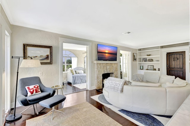 living room with visible vents, crown molding, wood finished floors, a fireplace, and a textured wall