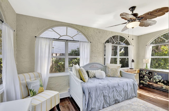 bedroom featuring wood finished floors, a textured wall, and ceiling fan