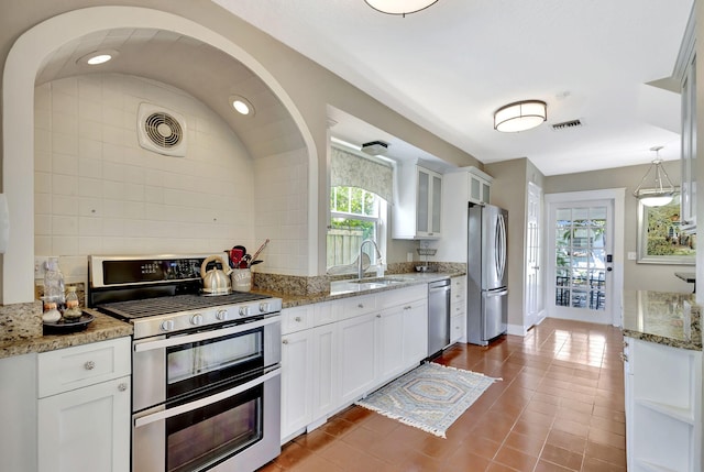 kitchen featuring glass insert cabinets, light stone countertops, appliances with stainless steel finishes, white cabinetry, and a sink