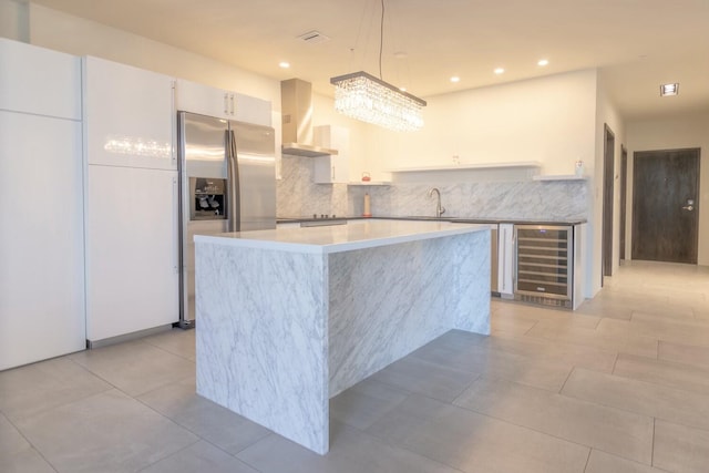 kitchen with a kitchen island, wall chimney range hood, beverage cooler, light tile patterned floors, and stainless steel refrigerator with ice dispenser