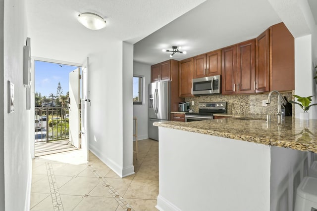 kitchen with light tile patterned floors, decorative backsplash, appliances with stainless steel finishes, a sink, and baseboards