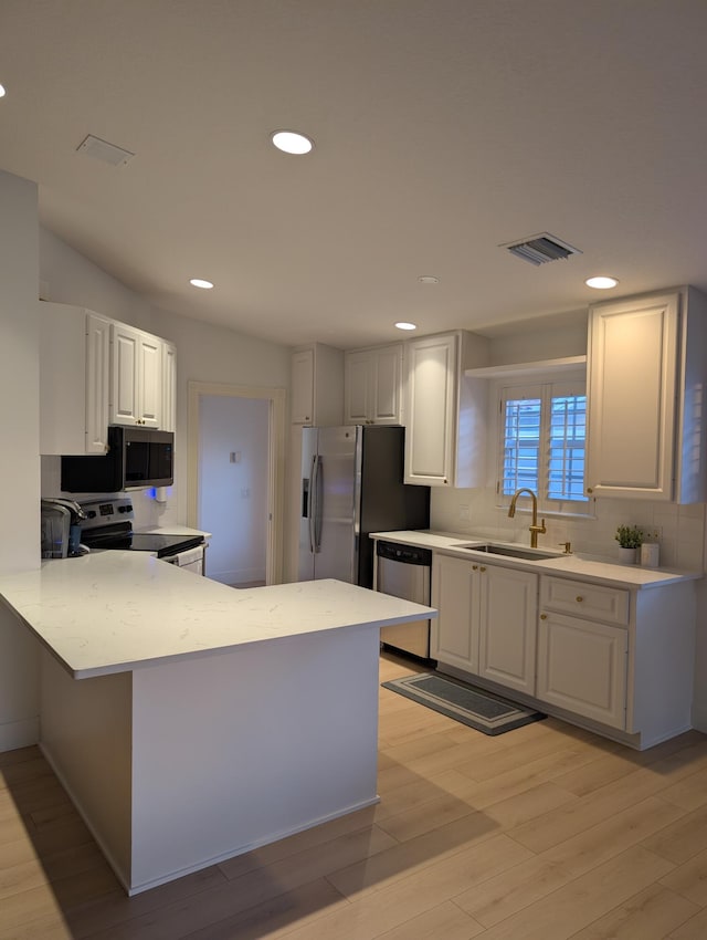 kitchen with light wood finished floors, a peninsula, a sink, appliances with stainless steel finishes, and tasteful backsplash