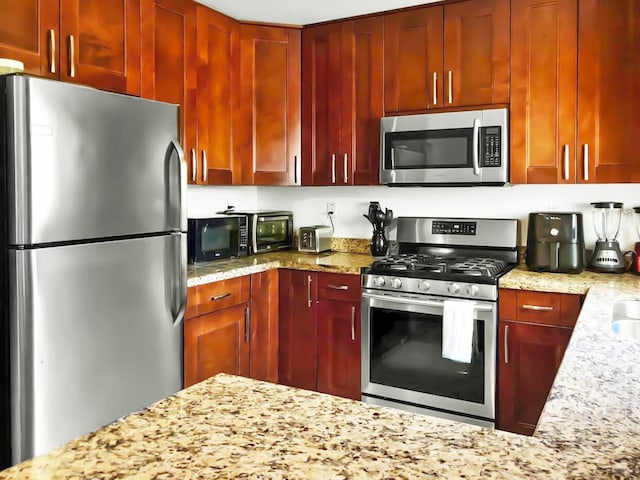 kitchen with reddish brown cabinets, light stone countertops, and appliances with stainless steel finishes