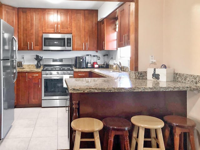 kitchen with light tile patterned floors, appliances with stainless steel finishes, light stone counters, a peninsula, and a sink