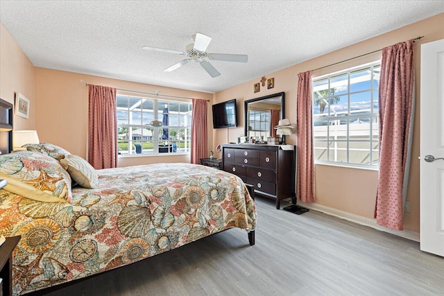 bedroom featuring a ceiling fan, a textured ceiling, baseboards, and wood finished floors