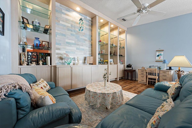 living room featuring built in shelves, visible vents, ceiling fan, a textured ceiling, and wood finished floors