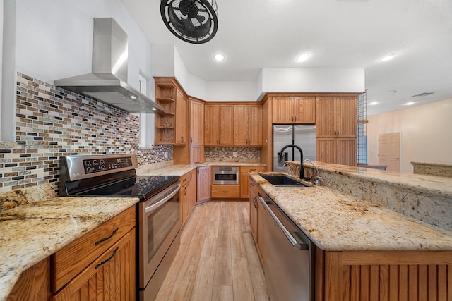 kitchen featuring light wood finished floors, a sink, wall chimney range hood, appliances with stainless steel finishes, and open shelves