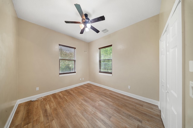 empty room with visible vents, light wood-style flooring, a ceiling fan, and baseboards