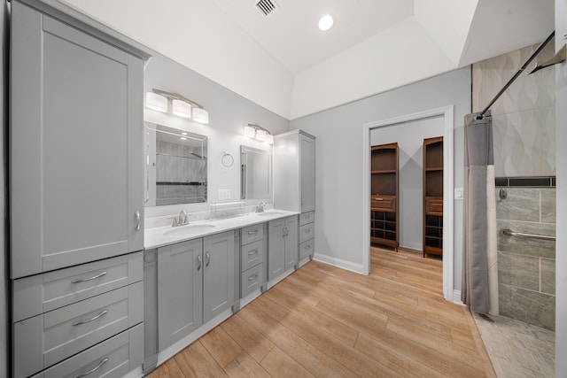 bathroom with visible vents, a sink, wood finished floors, double vanity, and tiled shower