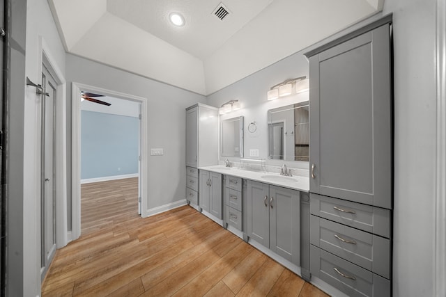 full bath featuring visible vents, a sink, wood finished floors, double vanity, and baseboards