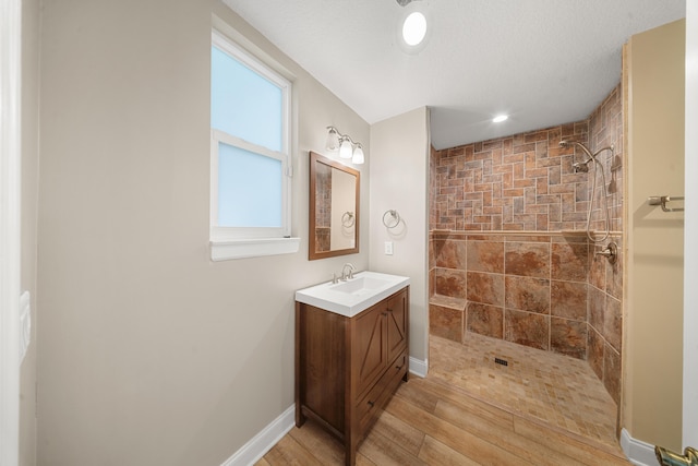 bathroom featuring a tile shower, vanity, baseboards, and wood finished floors