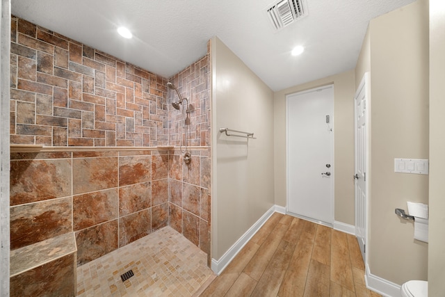 bathroom featuring visible vents, baseboards, toilet, tiled shower, and wood finished floors