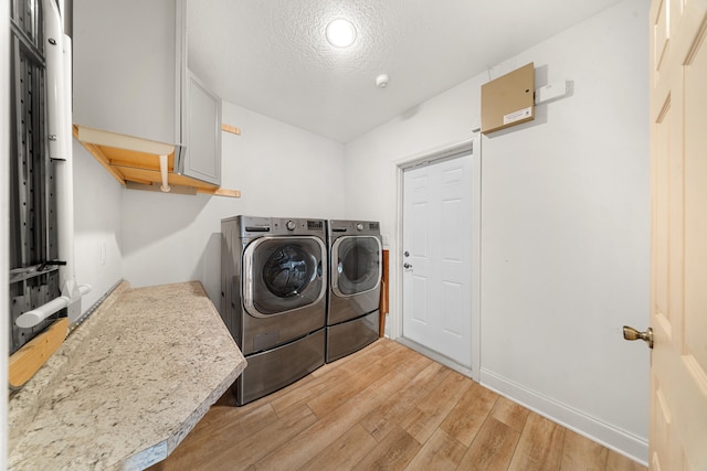 laundry area featuring a textured ceiling, washing machine and dryer, cabinet space, light wood finished floors, and baseboards