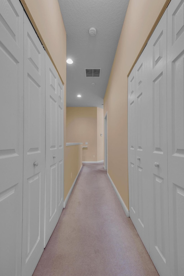 hallway with light carpet, visible vents, baseboards, and a textured ceiling