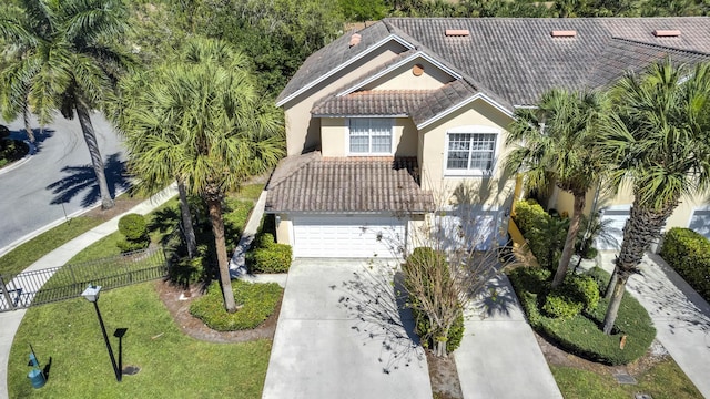 mediterranean / spanish-style home featuring a garage, concrete driveway, a tile roof, fence, and stucco siding