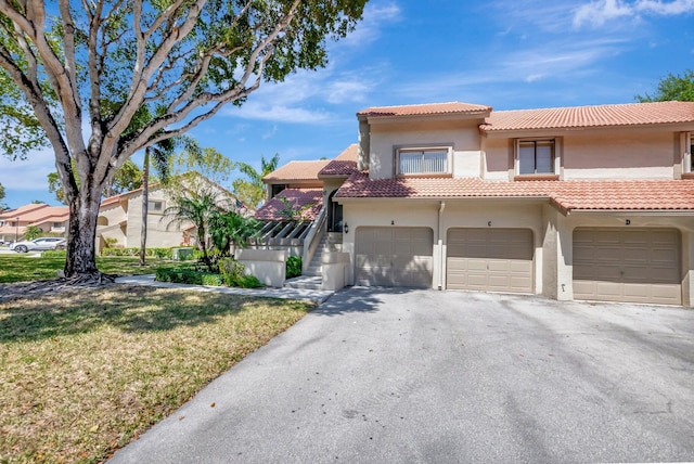 view of front of property featuring a garage, a tiled roof, driveway, stucco siding, and a front lawn