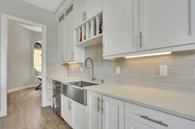 kitchen with tasteful backsplash, light wood finished floors, light countertops, white cabinetry, and a sink