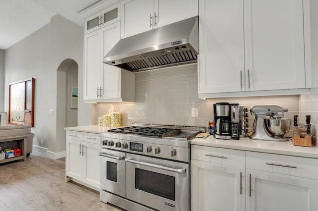 kitchen featuring double oven range, arched walkways, light countertops, under cabinet range hood, and backsplash