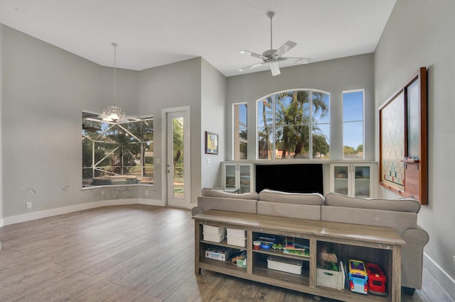 living area with baseboards, wood finished floors, and ceiling fan with notable chandelier