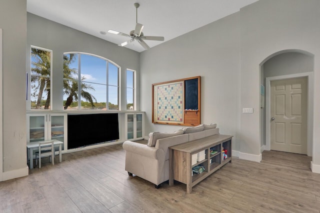 sitting room with arched walkways, ceiling fan, baseboards, and wood finished floors