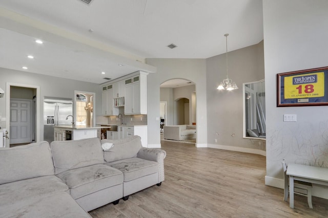 living room with baseboards, a chandelier, recessed lighting, light wood-style floors, and arched walkways