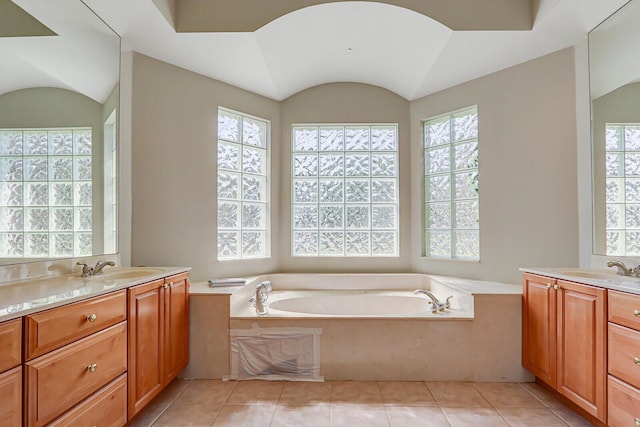 bathroom with tile patterned floors, two vanities, a sink, a bath, and vaulted ceiling