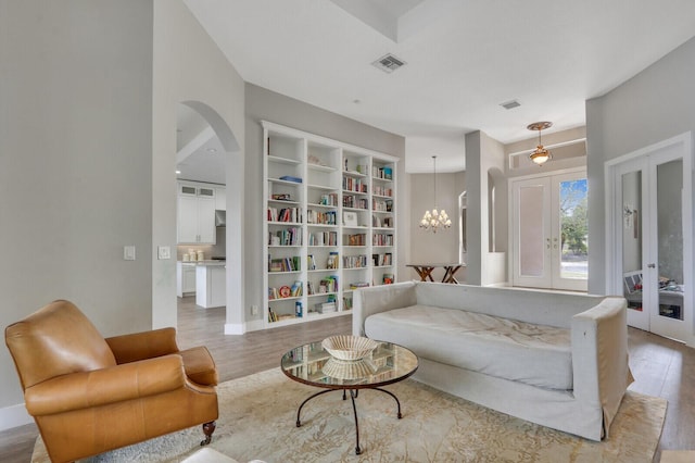 living area featuring wood finished floors, visible vents, arched walkways, french doors, and a notable chandelier