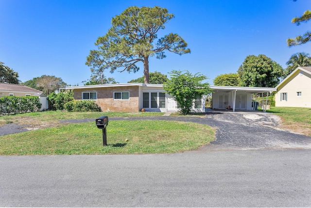 view of front of home featuring brick siding, aphalt driveway, an attached carport, and a front yard